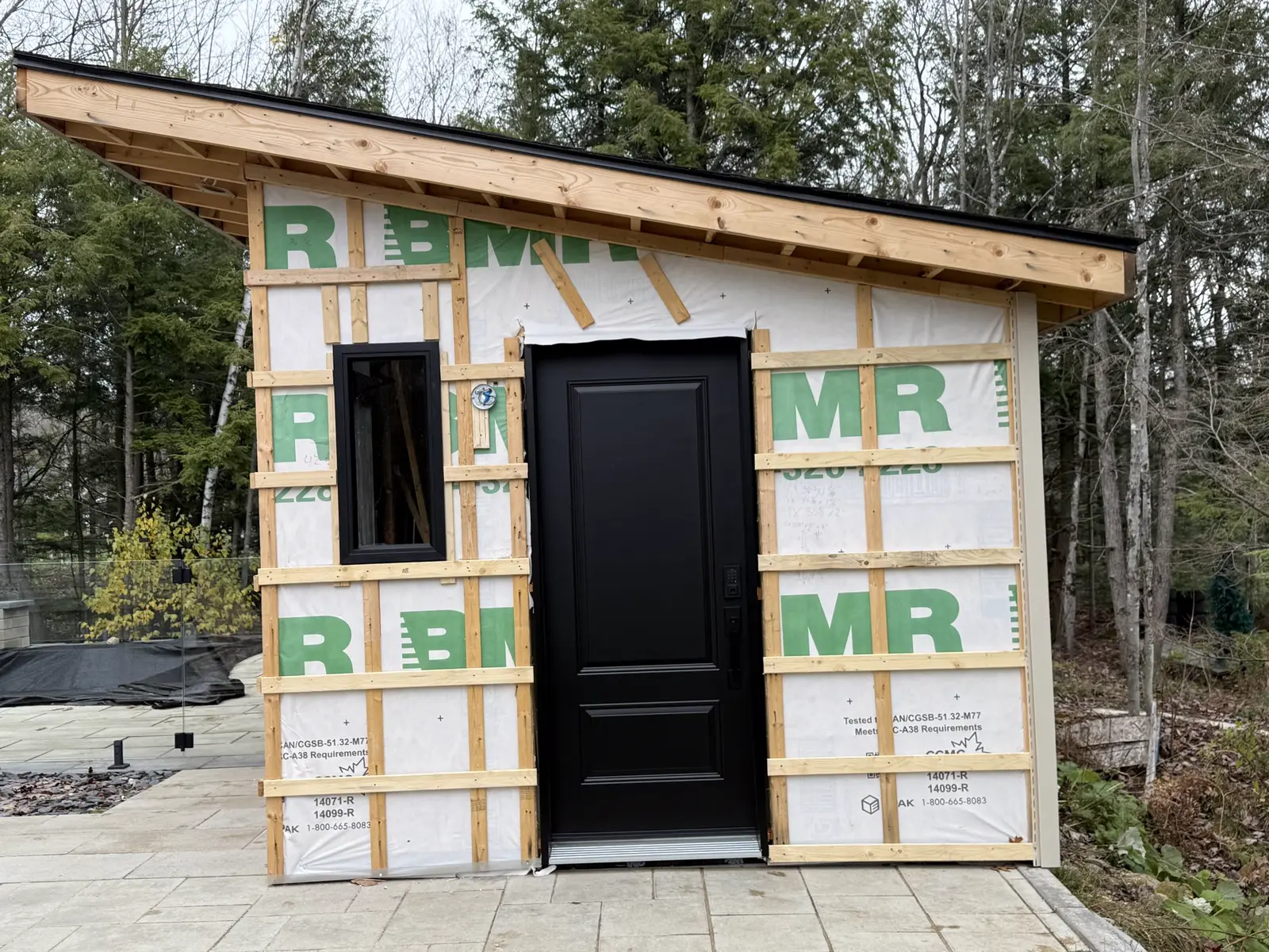 Small building with house wrap installed and a black door in place, a PRO G2 project